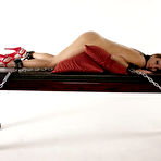 Pic of Blonde Mistress in latex clothing forces a slave to orgasm on bondage table